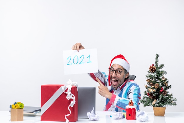 Widok z przodu męski pracownik siedzący w swoim miejscu pracy, trzymający kartkę papieru z numerem 2021, koncepcja nowego roku