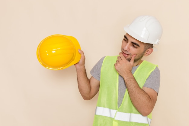 Bezpłatne zdjęcie widok z przodu mężczyzna budowniczy w białym kasku, trzymając żółty na kremowym tle