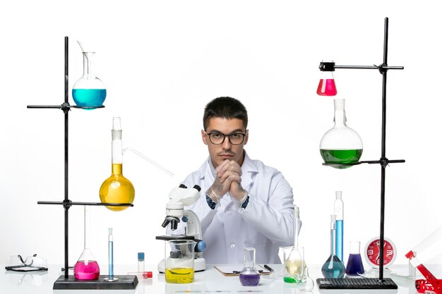Widok z przodu mężczyzna chemik w białym garniturze medycznym siedzi z roztworami na białym tle laboratorium naukowe wirusa choroby Covid