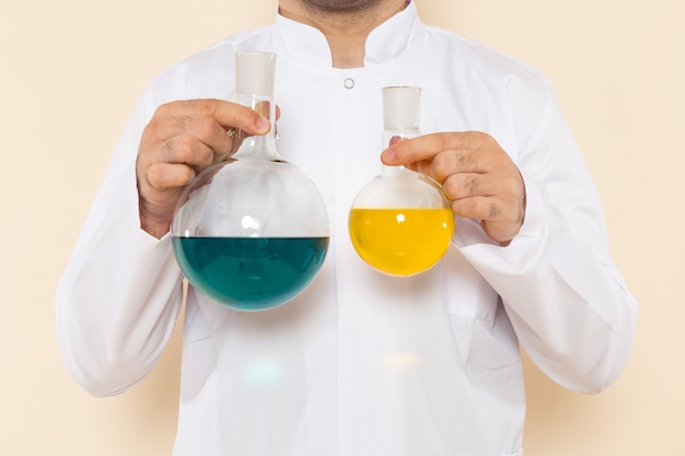 Widok z przodu mężczyzna chemik w białym specjalnym garniturze trzymający kolby roztworów na biurku z kremem laboratorium naukowe eksperyment chemia naukowa
