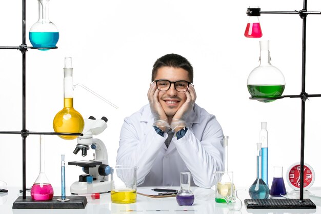 Widok z przodu mężczyzna chemik w garniturze medycznym siedzi i uśmiecha się na białym tle nauka o chorobach wirusowych covid splash