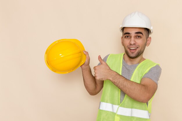 Bezpłatne zdjęcie widok z przodu mężczyzna konstruktor w białym kasku, trzymając żółty kask na jasnym tle