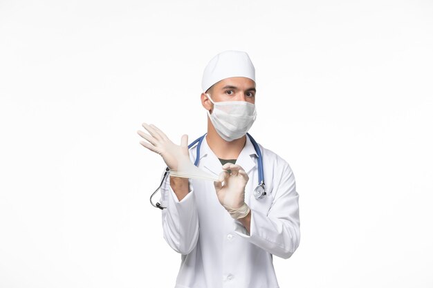 Widok z przodu mężczyzna lekarz w kombinezonie medycznym i noszący maskę przeciwko covid na białej ścianie wirusa pandemii choroby