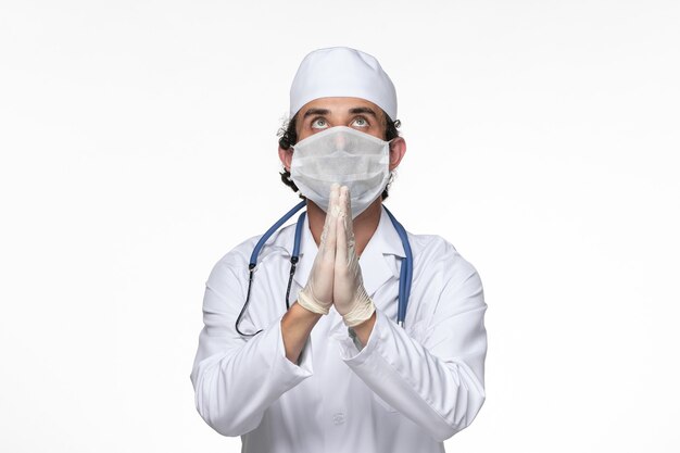 Widok z przodu mężczyzna lekarz w kombinezonie medycznym w masce jako ochrona przed covid - modląc się na białej ścianie choroba wirusowa zdrowie covid - pandemia