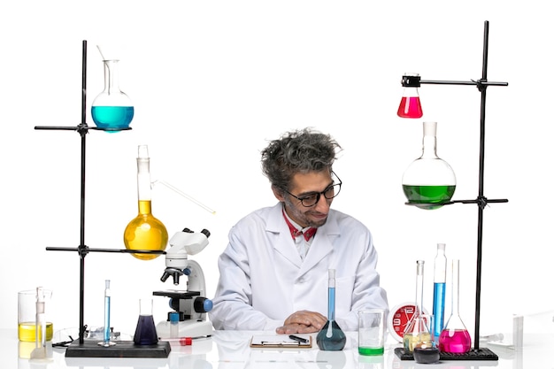 Widok z przodu mężczyzna naukowiec w białym garniturze medycznym siedzi przed stołem z roztworami