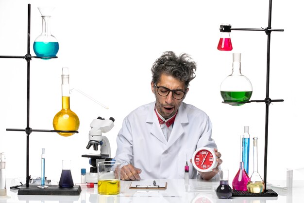 Widok z przodu mężczyzna naukowiec w kombinezonie medycznym trzymający zegary na jasnobiałym tle chemia zdrowie wirus covid-lab