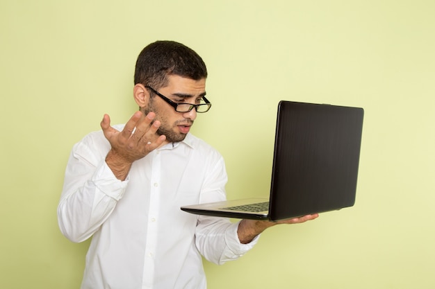 Widok z przodu mężczyzna pracownik biurowy w białej koszuli za pomocą swojego laptopa na zielonej ścianie