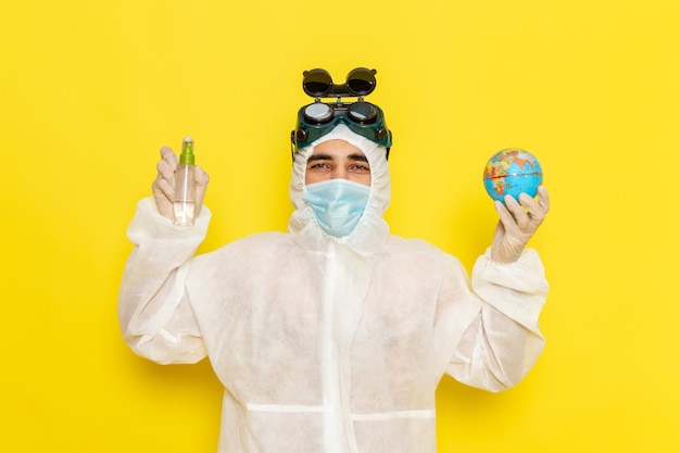 Bezpłatne zdjęcie widok z przodu mężczyzna pracownik naukowy w specjalnym garniturze, trzymając mały okrągły glob i spray na żółtym biurku