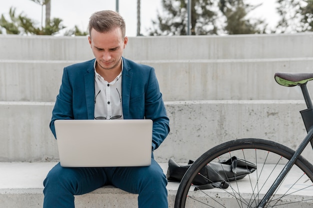 Bezpłatne zdjęcie widok z przodu mężczyzna pracujący na laptopie obok swojego roweru