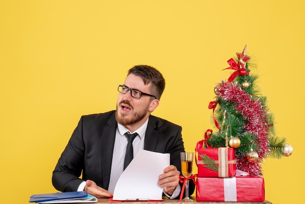 Widok z przodu mężczyzna robotnik za stołem z prezentami i Boże Narodzenie drzewo na żółto