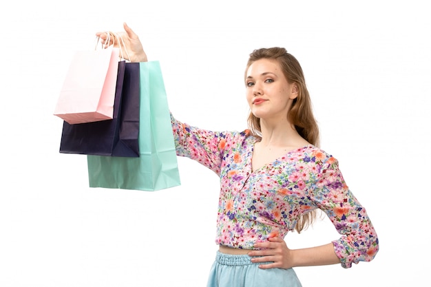 Bezpłatne zdjęcie widok z przodu młoda atrakcyjna dama w koszuli zaprojektowane w kolorowe kwiatki i niebieskiej spódnicy, trzymając pakiety zakupów na białym