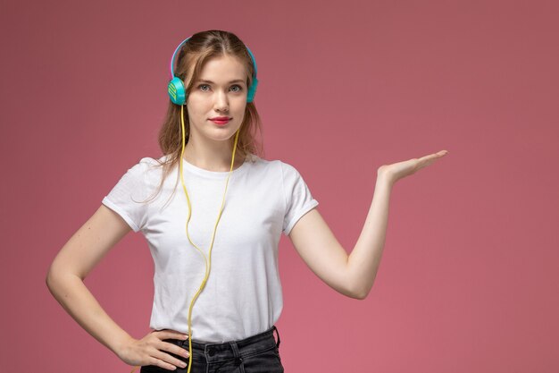 Widok z przodu młoda atrakcyjna kobieta słuchanie muzyki w słuchawkach na ciemnoróżowej ścianie kolor modelu samica młoda dziewczyna