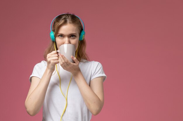 Widok z przodu młoda atrakcyjna kobieta w białej koszulce pije herbatę słuchając muzyki na różowej ścianie kolor modelu samica młoda