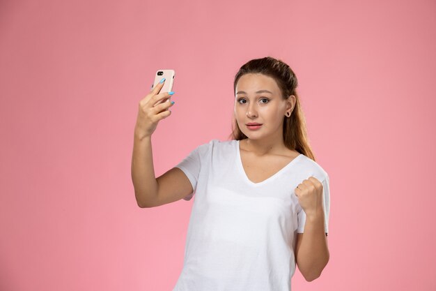 Widok z przodu młoda atrakcyjna kobieta w białej koszulce robienia selfie na różowym tle