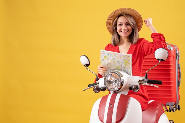 Widok z przodu młoda dama na motorowerze z czerwoną walizką trzymającą mapę pokazującą mięśnie ramienia