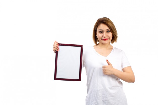 Widok z przodu młoda dama w białej koszulce trzyma burgundową ramkę na zdjęcia uśmiecha się na białym tle