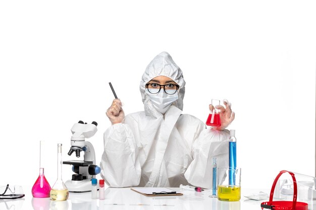Widok z przodu młoda kobieta chemik w specjalnym kombinezonie ochronnym, trzymając czerwony roztwór na białym tle laboratorium wirusów covid- chemistry