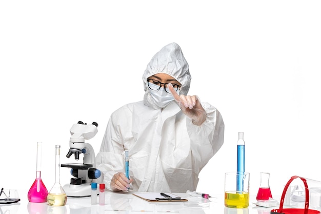 Widok Z Przodu Młoda Kobieta Chemik W Specjalnym Kombinezonie Ochronnym, Trzymając Kolbę Z Niebieskim Roztworem Na Jasnobiałym Tle Laboratorium Wirusów Chemii Covid