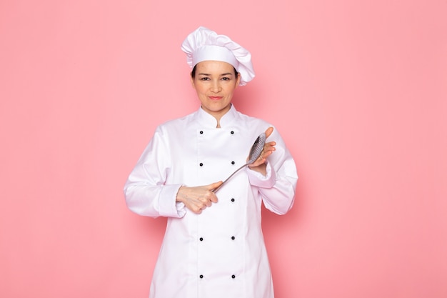 Widok z przodu młoda kobieta kucharz w białym garniturze gotować białą czapkę pozowanie gospodarstwa duże srebrne łyżki