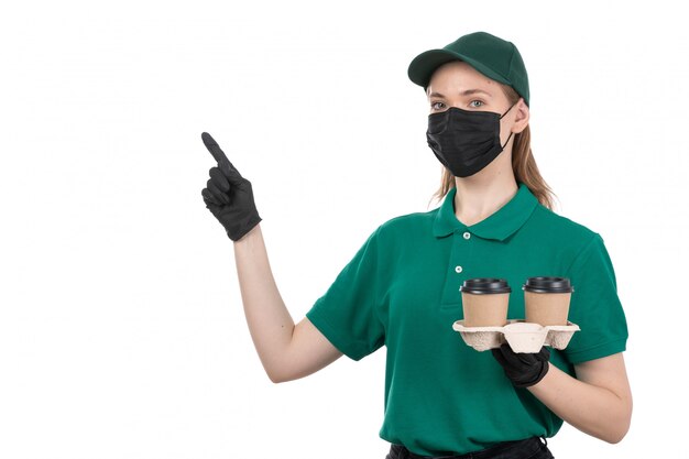 Widok z przodu młoda kobieta kurier w zielone jednolite czarne rękawiczki i czarną maskę trzyma filiżanki kawy