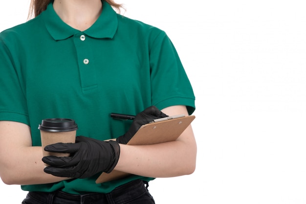 Widok z przodu młoda kobieta kurier w zielonych jednolitych czarnych rękawiczkach i czarnej masce trzyma filiżankę kawy i notatnik