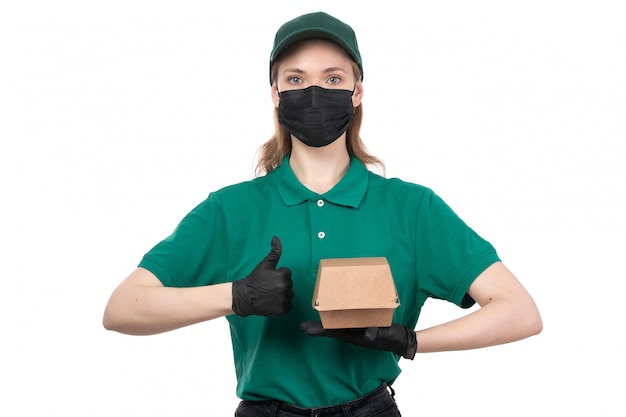 Widok z przodu młoda kobieta kurier w zielonych jednolitych czarnych rękawiczkach i czarnej masce trzyma pakiet dostawy żywności