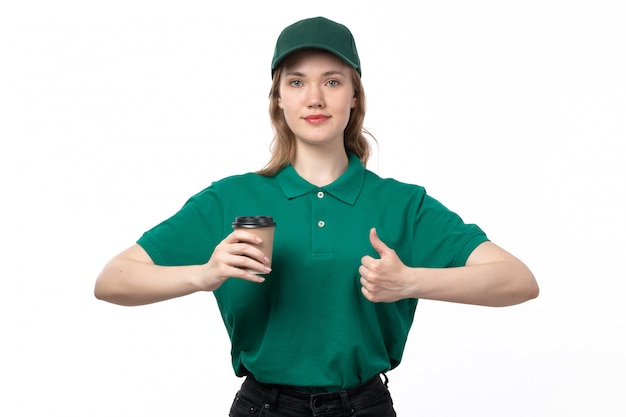Widok z przodu młoda kobieta kurier w zielonym mundurze, trzymając filiżankę kawy i uśmiechając się na białym tle