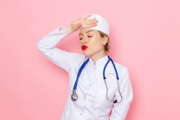 Widok z przodu młoda kobieta lekarz w białym garniturze z niebieskim stetoskopem pozowanie na różowej przestrzeni pracy kobiet
