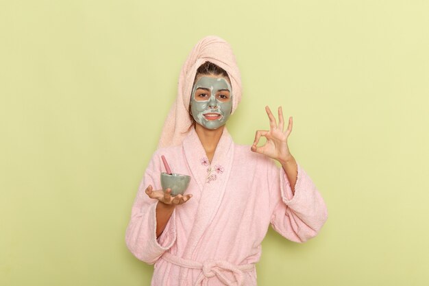 Widok z przodu młoda kobieta po prysznicem w różowym szlafroku trzymając miskę z maską na zielonej powierzchni
