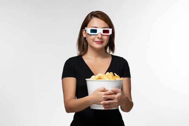 Widok z przodu młoda kobieta trzyma chipsy d okulary przeciwsłoneczne i uśmiecha się na białej powierzchni