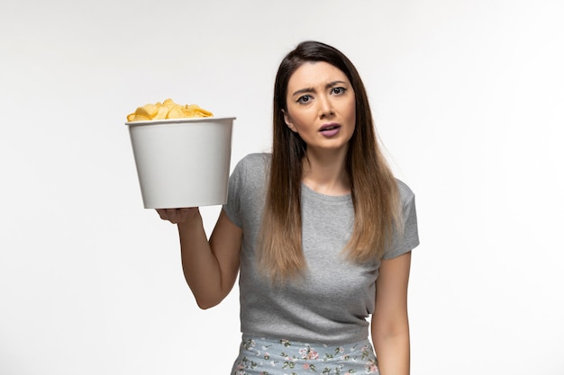 Widok z przodu młoda kobieta trzyma chipsy ziemniaczane podczas oglądania filmu na białym piętrze filmów kinowych zdalnego samotna kobieta