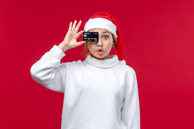 Widok z przodu młoda kobieta trzyma kartę bankową na czerwonej podłodze czerwone święto pieniędzy na Boże Narodzenie