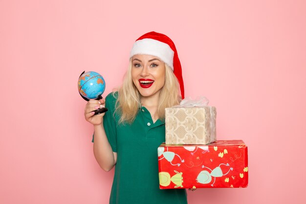 Widok z przodu młoda kobieta trzyma kulę ziemską i prezenty świąteczne na różowej ścianie zdjęcie model kobieta boże narodzenie nowy rok kolor wakacje