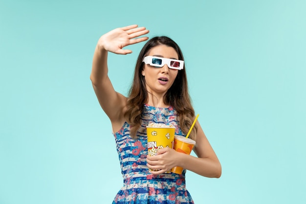 Widok z przodu młoda kobieta trzyma napój popcorn w d okulary przeciwsłoneczne na jasnoniebieskiej powierzchni