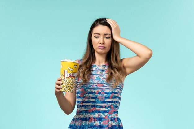 Widok z przodu młoda kobieta trzyma pakiet popcornu jedzenie na niebieskiej powierzchni