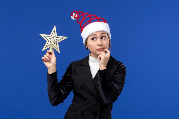Widok z przodu młoda kobieta trzyma wystrój w kształcie gwiazdy na niebieskiej ścianie nowy rok wakacje kobieta