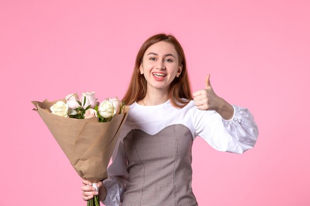 Widok z przodu młoda kobieta trzymająca bukiet pięknych róż pokazująca niesamowity gest na różu