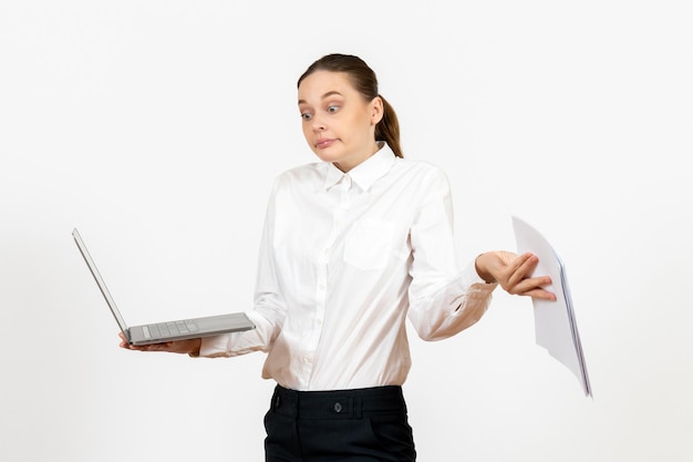 Widok z przodu młoda kobieta w białej bluzce trzymająca laptopa i dokumenty na jasnym białym tle model uczucia kobiecego biura pracy
