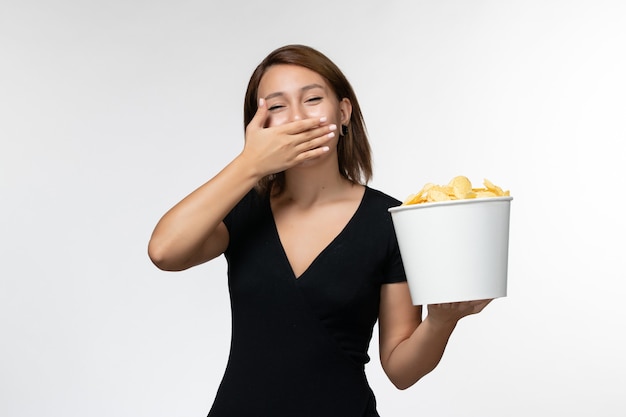 Widok z przodu młoda kobieta w czarnej koszuli trzymając chipsy ziemniaczane i śmiejąc się na białej powierzchni