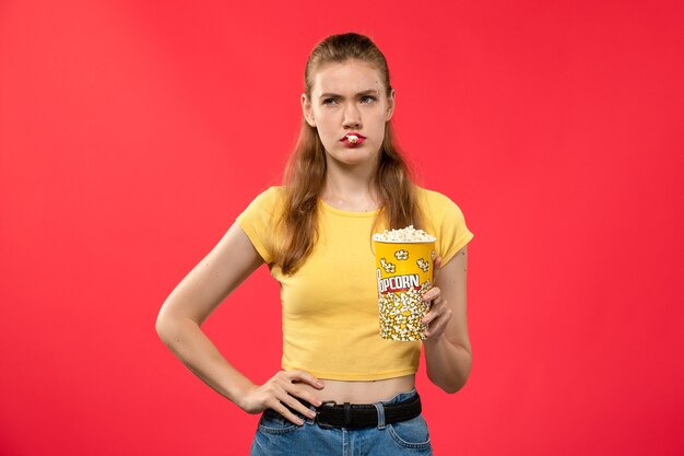 Widok z przodu młoda kobieta w kinie trzymając pakiet popcornu i pozowanie na czerwonej ścianie kino teatr kino kobiece zabawa film