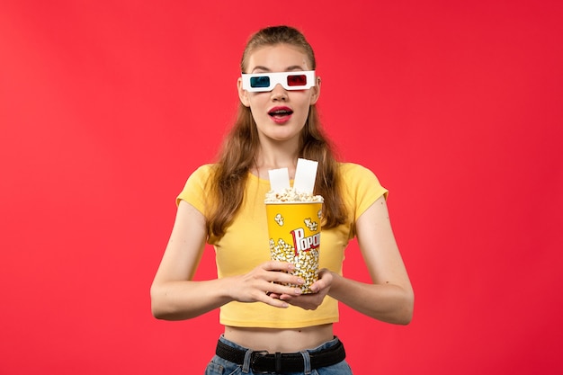 Widok Z Przodu Młoda Kobieta W Kinie Trzymając Pakiet Popcornu W Okularach Przeciwsłonecznych, Trzymając Bilety Na Czerwonym Biurku Kino Kino Dziewczyna Film