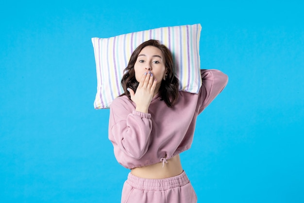Widok z przodu młoda kobieta w różowej piżamie trzymająca poduszkę na niebieskiej ścianie noc kolor bezsenność łóżko odpoczynek sen kobieta impreza emocje sen