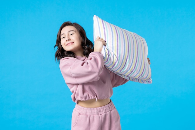 Widok z przodu młoda kobieta w różowej piżamie trzymająca poduszkę na niebieskiej ścianie noc kolor łóżko odpoczynek emocje sen sen bezsenność