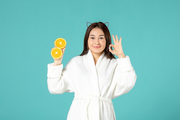 widok z przodu młoda kobieta w szlafroku trzymająca pokrojoną pomarańczę na niebieskim tle