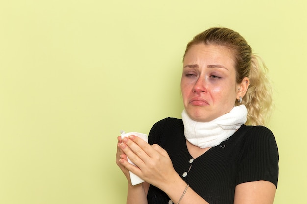 Bezpłatne zdjęcie widok z przodu młoda kobieta z białym ręcznikiem wokół gardła, czuje się bardzo chora i chora na jasnozielonej ścianie choroba choroba kolor kobiet zdrowie