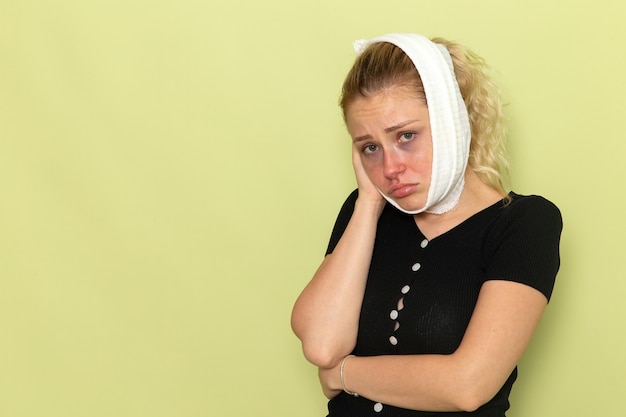 Widok z przodu młoda kobieta z białym ręcznikiem wokół głowy czuje się bardzo chora i chora na jasnozielonej ścianie choroba choroba dziewczyna zdrowie kobiety