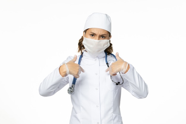 Widok z przodu młoda lekarka ze sterylną maską i rękawiczkami z powodu koronawirusa na jasnobiałej powierzchni