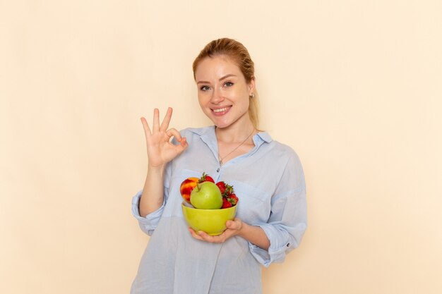 Widok z przodu młoda piękna kobieta w koszuli trzymając talerz z owocami uśmiechając się na ścianie kremu stanowią dojrzałe kobiety modelki owoców