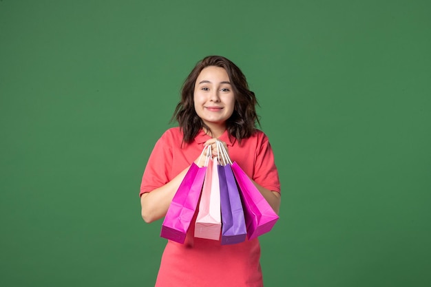 Bezpłatne zdjęcie widok z przodu młoda sprzedawczyni trzymająca pakiety prezentów na zielonym tle praca pracownik butik wyprzedaż prezent zakupy jednolite emocje