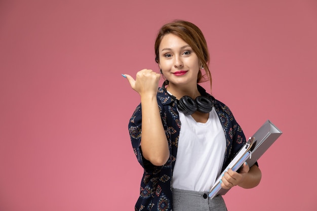 Widok z przodu młoda studentka w białej koszulce i szarych spodniach trzyma dokument z uśmiechem na różowym tle lekcje dla studentów uczelni